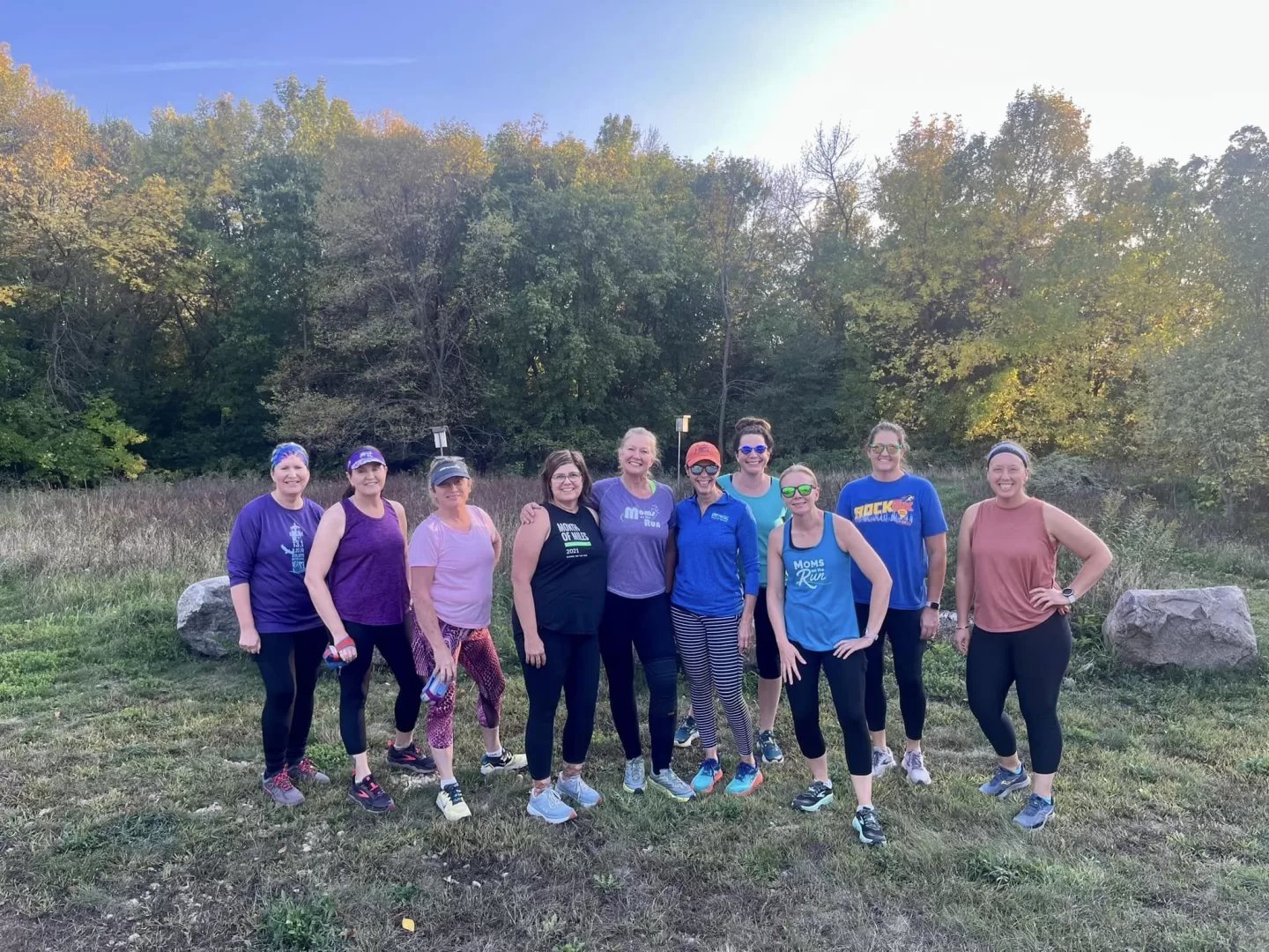 10 Burnsville Moms on the Run runners standing on the grass in front of trees