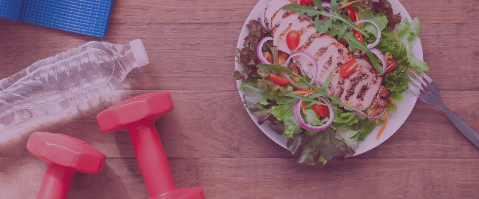 white bowl with salad on right, corner of blue yoga mat, water bottle and orange dumbbells on left